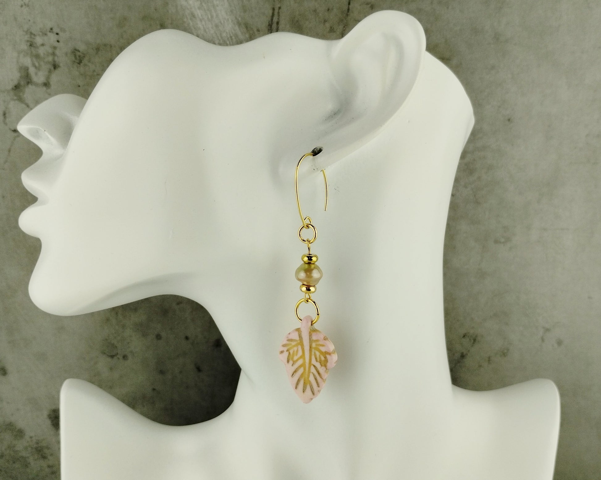 Gold earrings with pink floral design on a white mannequin ear against a gray background