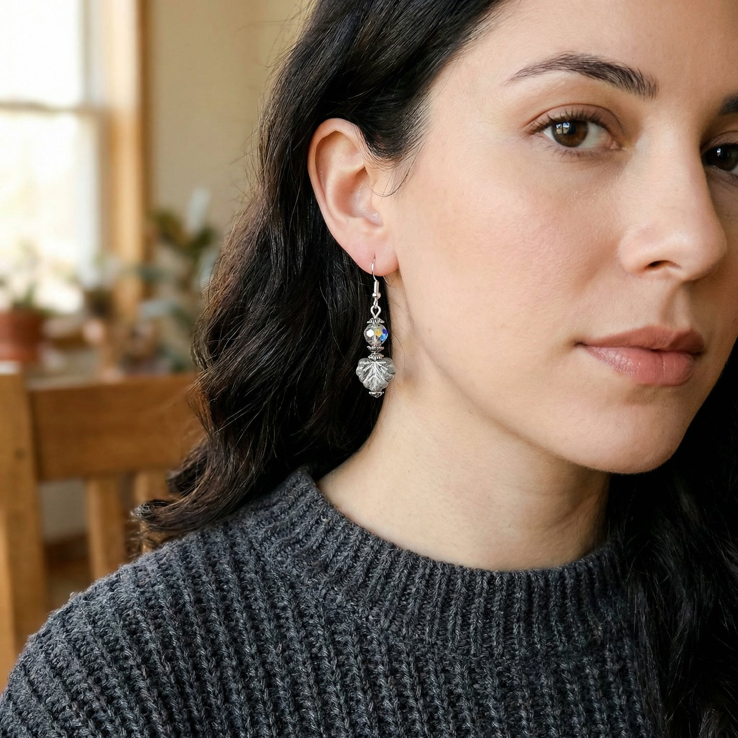 Close-up of a woman wearing a silver earring with a leaf-shaped bead.