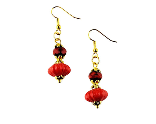 A pair of dangling earrings with gold-tone fishhook wires, small faceted dark red beads, and larger glossy red bead drops with gold-tone caps, shown on a plain white background.