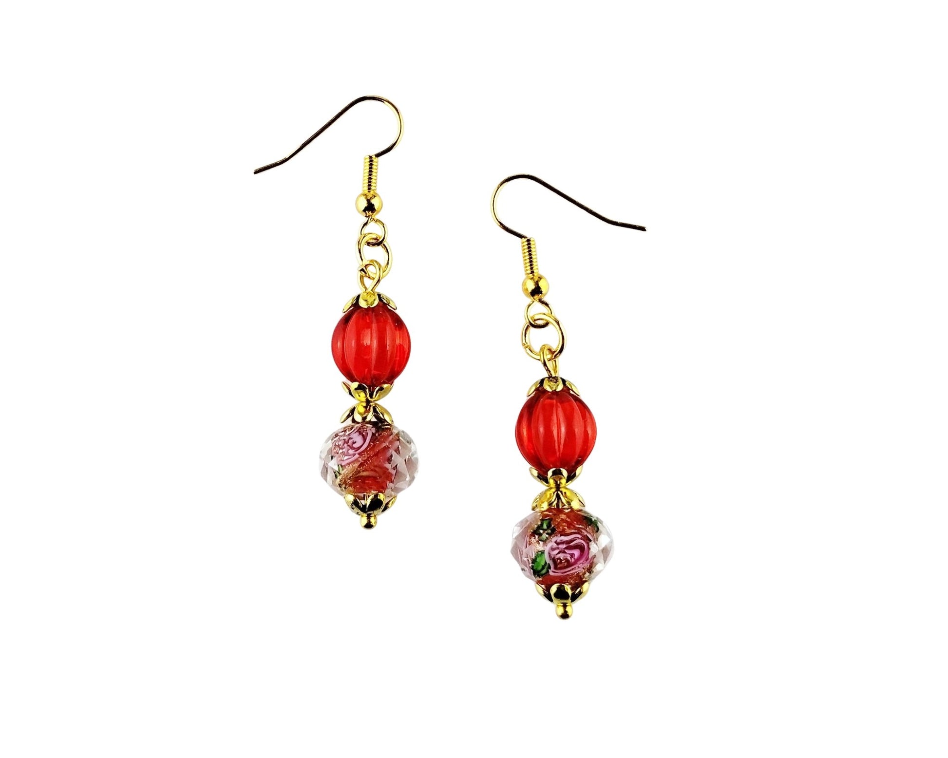 A pair of dangle earrings with gold-tone fishhook wires, a glossy red round bead, and a clear glass bead featuring a pink floral pattern, set against a plain white background.