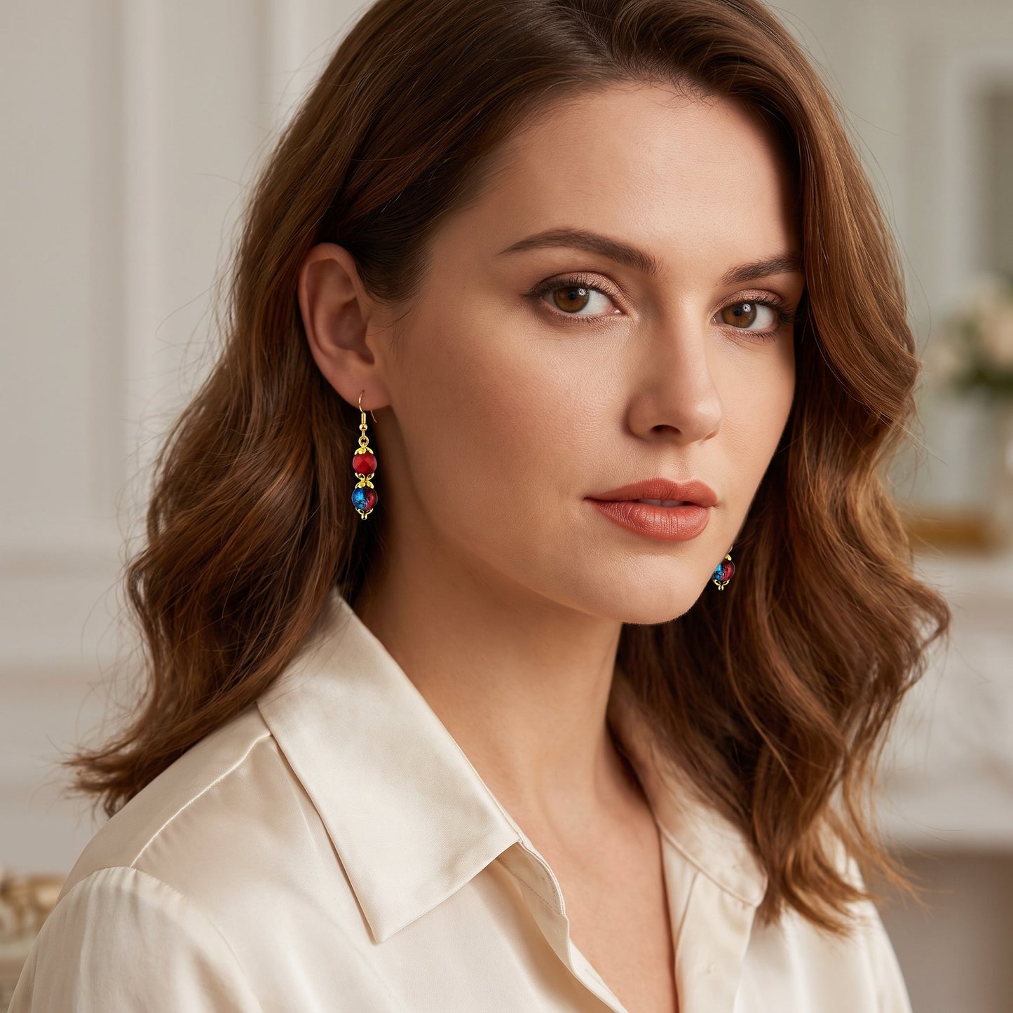 A woman with wavy brown hair wearing colorful dangling earrings and a cream-colored collared blouse, photographed in a softly lit indoor setting.