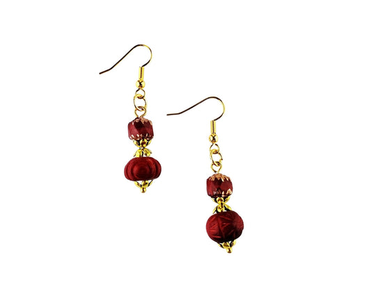 A pair of drop earrings featuring faceted deep red beads and gold-tone metal hooks, shown against a plain white background.