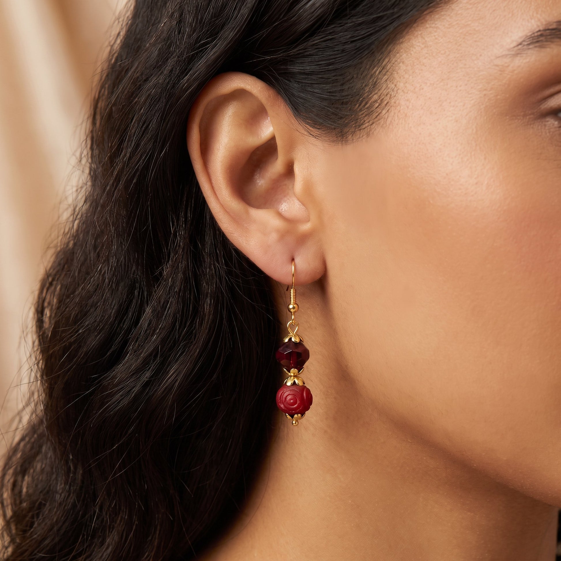 A close-up of a woman's ear wearing a dangling earring with gold-toned metal and deep red faceted beads.