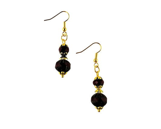 A pair of gold-tone dangle earrings with faceted dark red beads, shown against a plain white background.