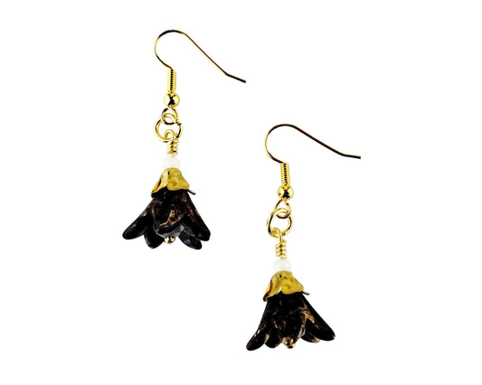 A pair of dangling earrings with gold fishhook wires and small gold-toned caps above dark, irregularly shaped drop charms, shown on a plain white background.