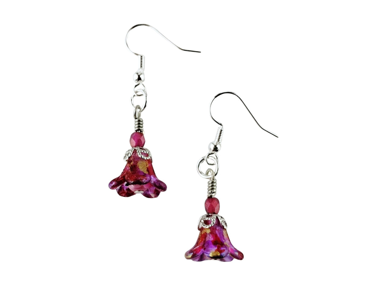 A pair of handmade dangle earrings featuring textured magenta glass flower charms with silver-tone metal wire hooks and beads, shown against a plain white background.