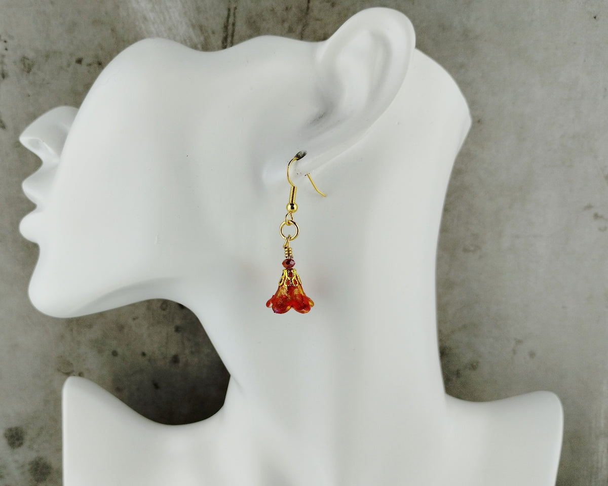 A single gold dangle earring with small red gemstone drops, displayed on a white mannequin head against a textured gray background.