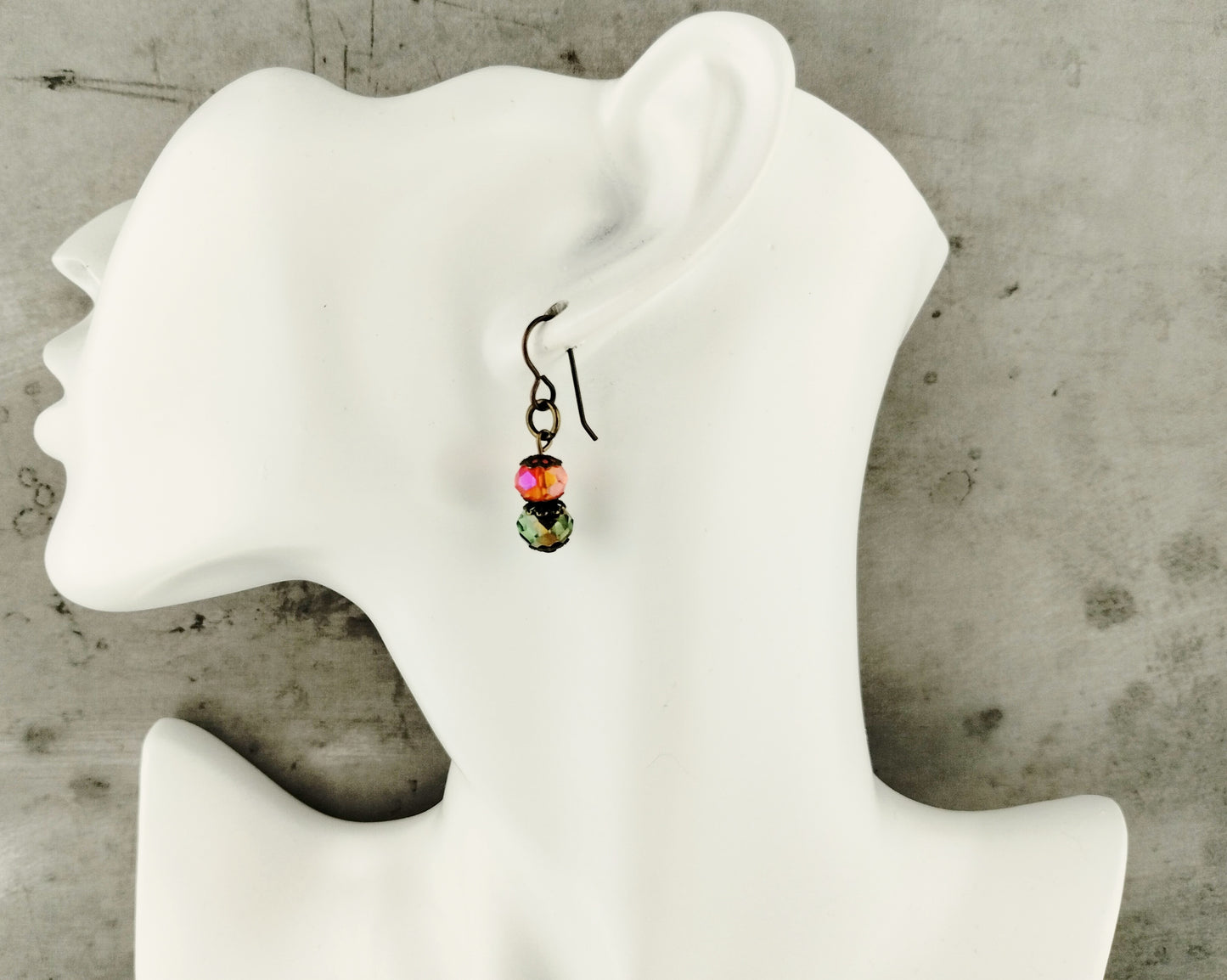 Earring with colorful beads on a white mannequin ear against a concrete wall background