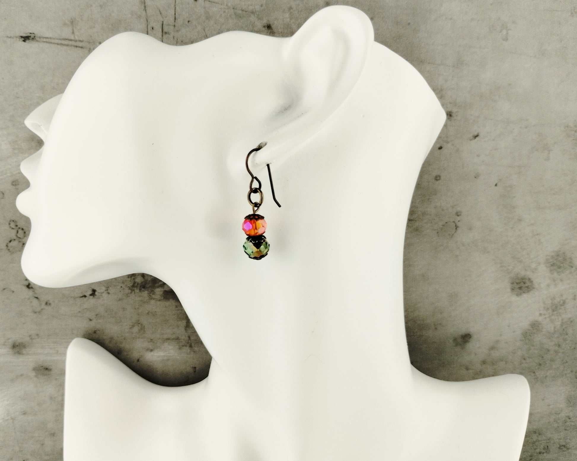 Earring with colorful beads on a white mannequin ear against a concrete wall background