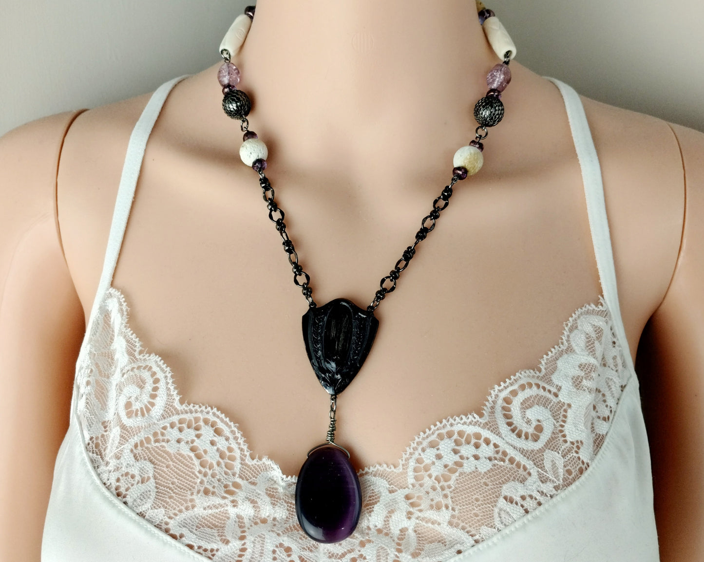 Necklace with a large purple pendant on a mannequin wearing a white lace top.