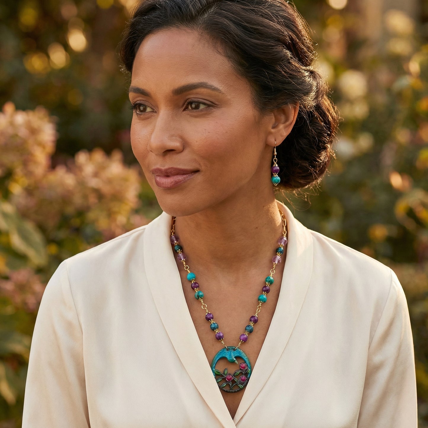 Woman wearing a colorful necklace outdoors with blurred greenery in the background