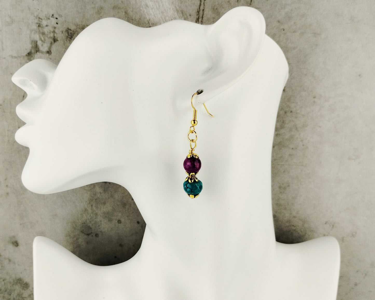 Earrings with purple and green beads on a mannequin ear against a neutral background