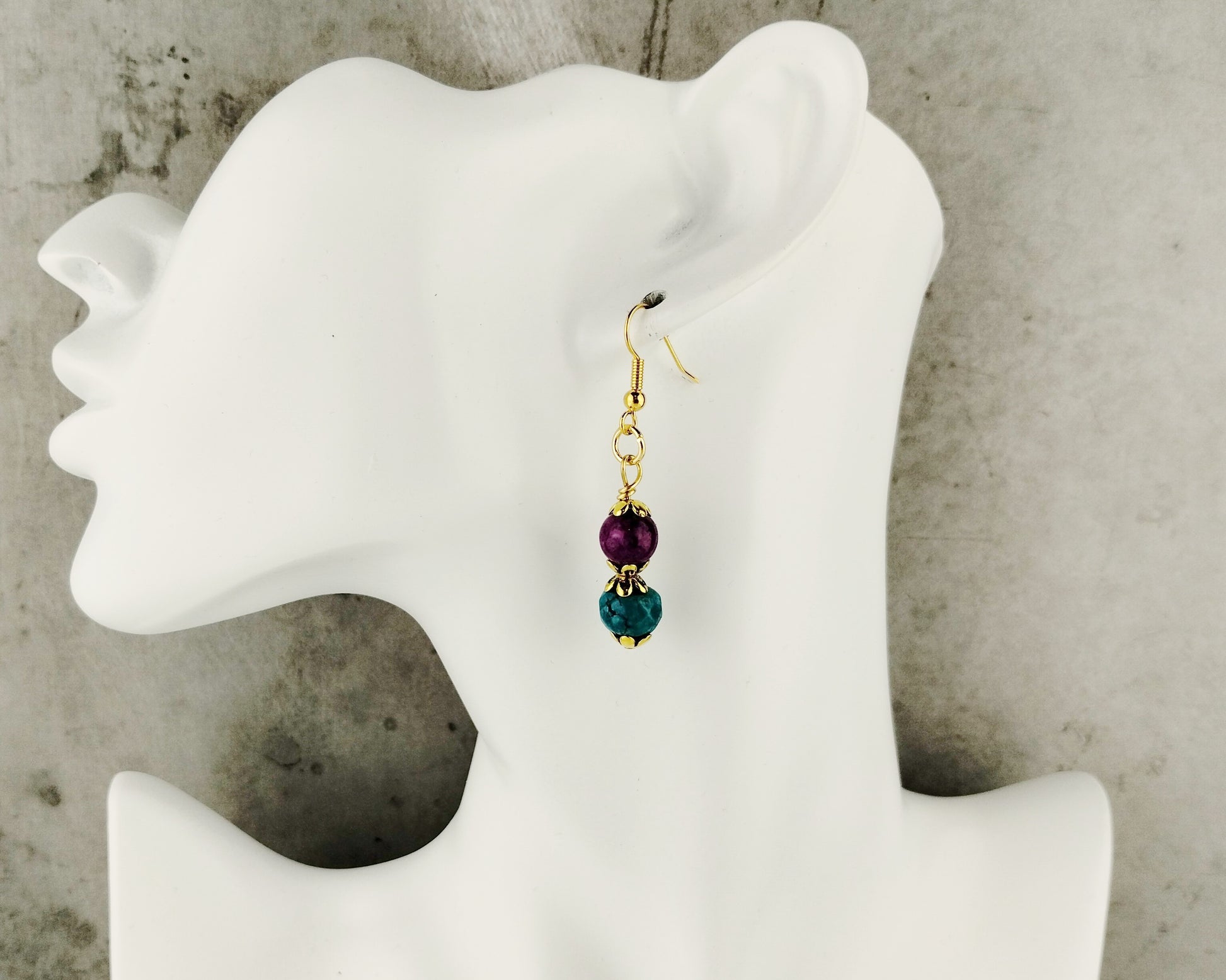 Earrings with purple and green beads on a mannequin ear against a neutral background