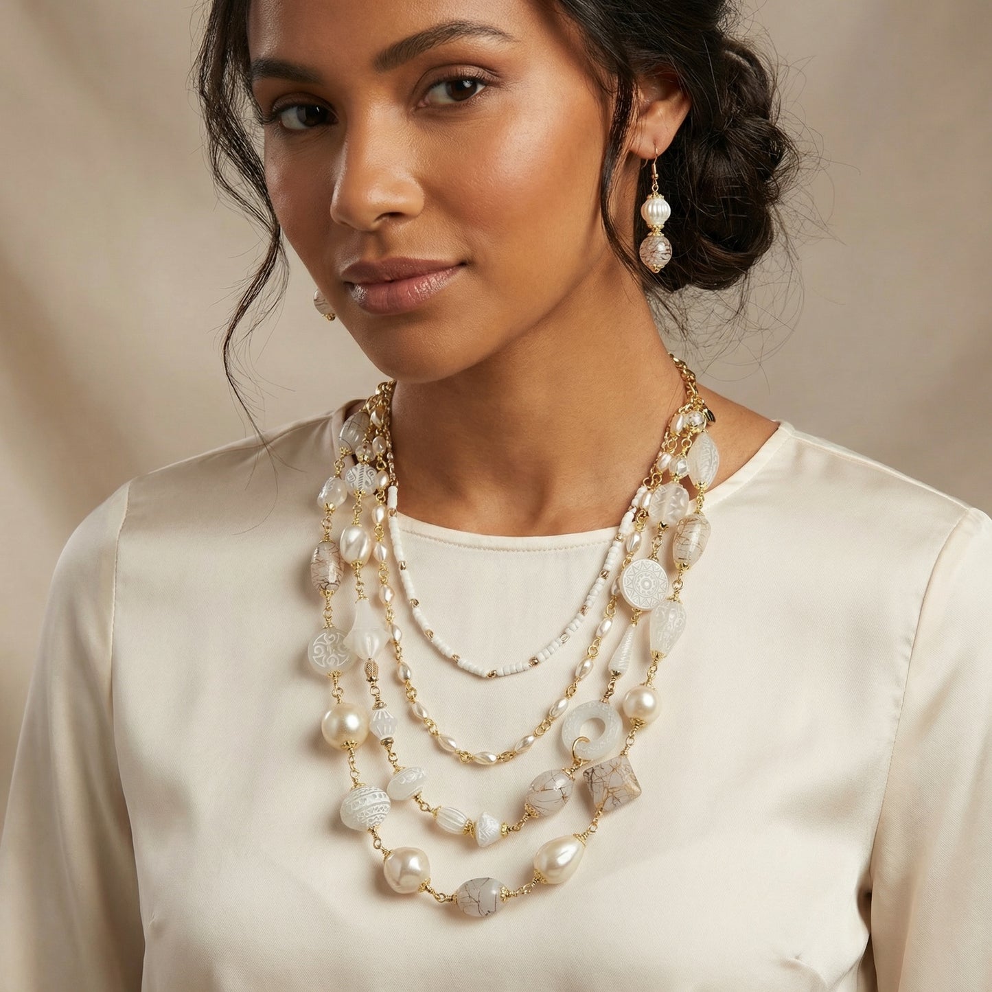 Woman wearing a layered pearl and gold necklace with earrings against a neutral background