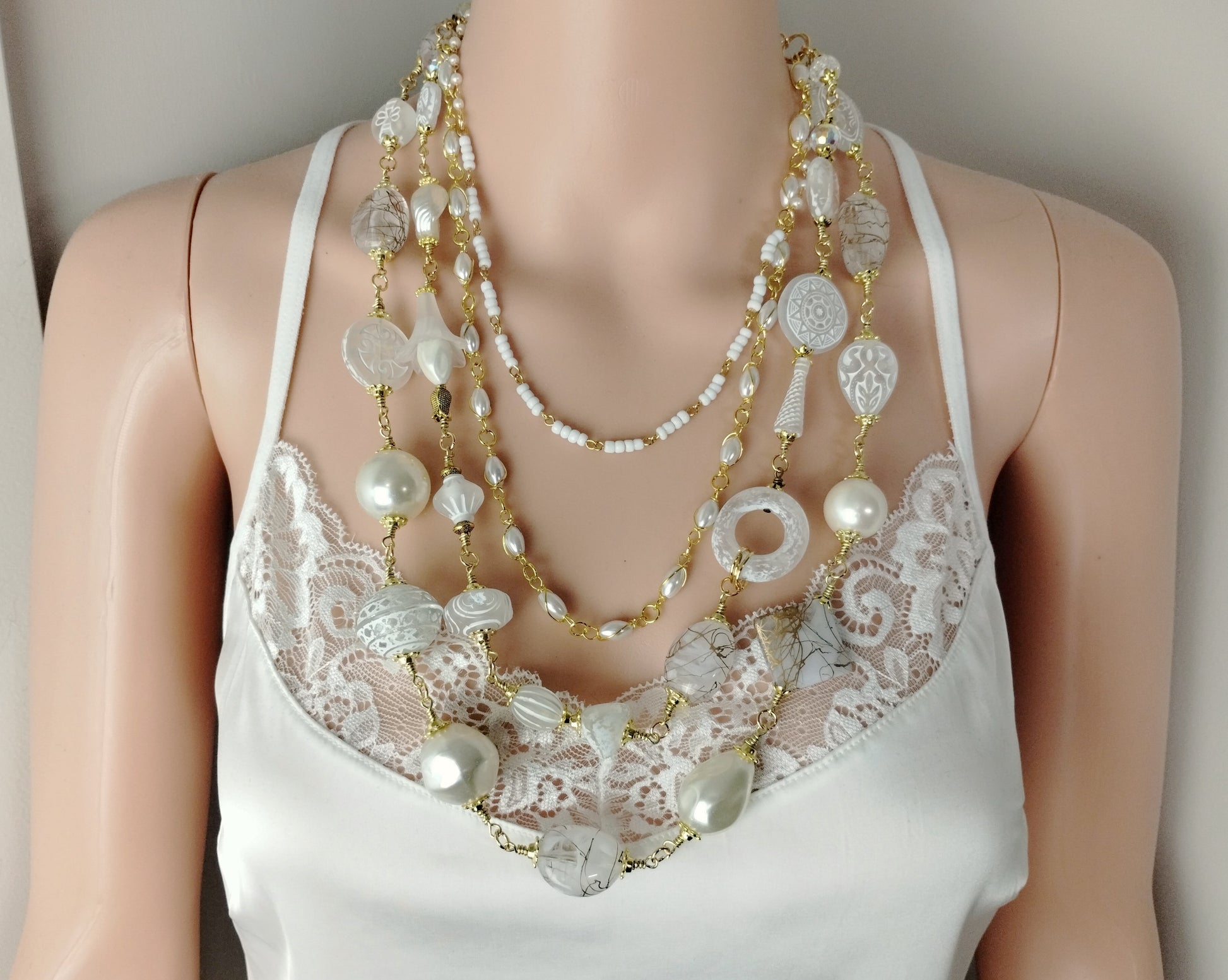 Mannequin wearing a white lace top with multiple layered necklaces on a neutral background