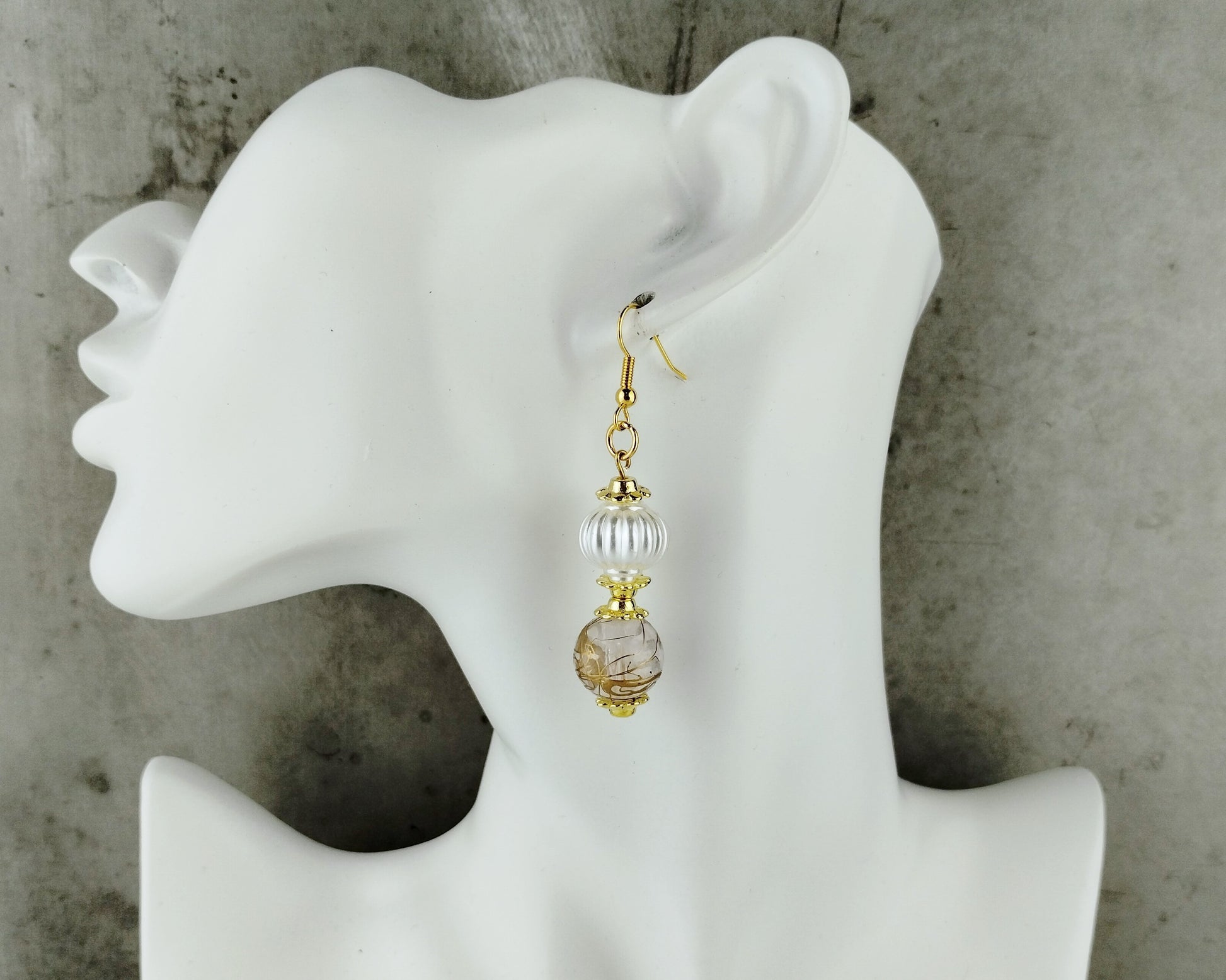 Gold and clear beaded earring on a white mannequin ear against a gray background