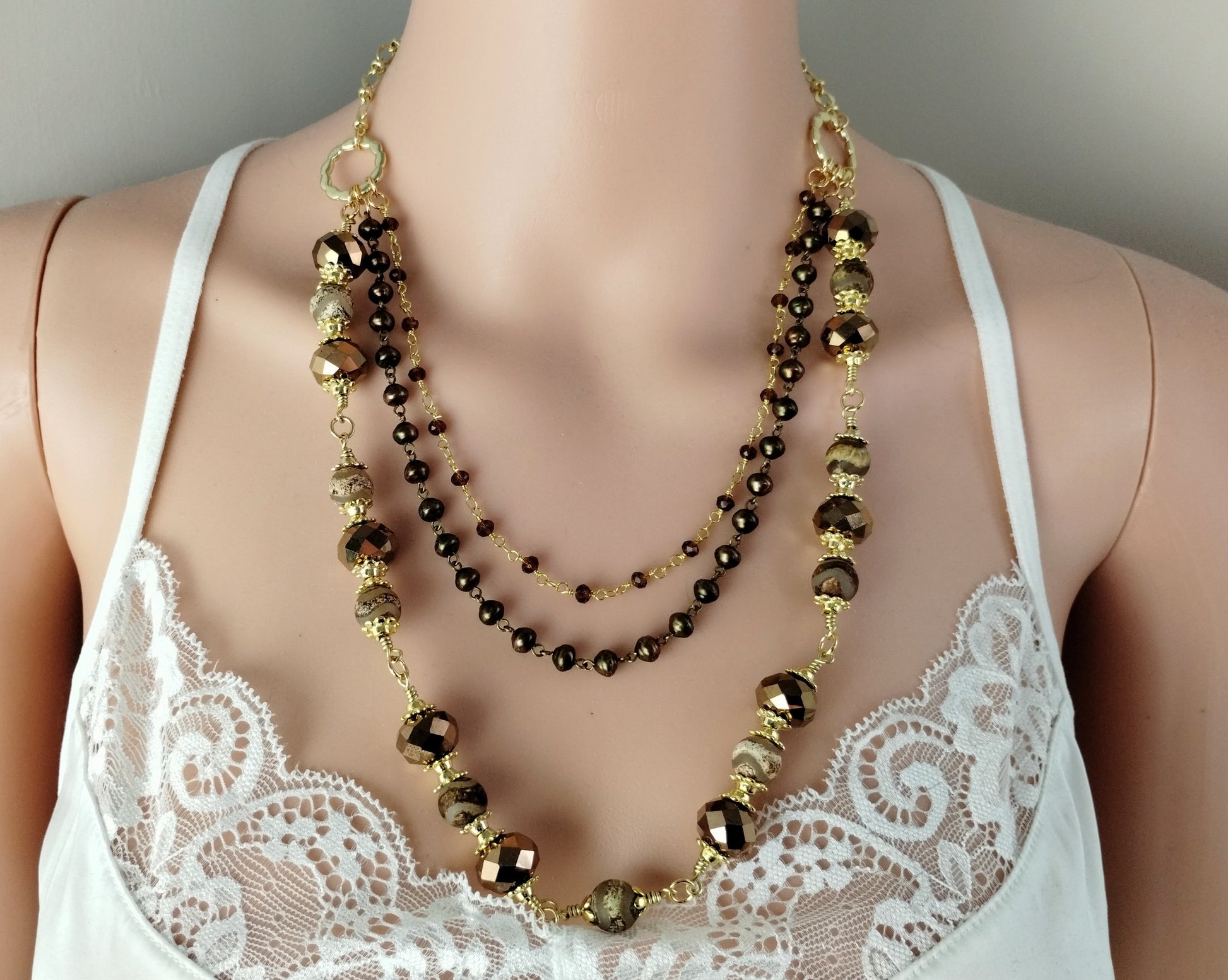 Necklace with gold and brown beads on a mannequin wearing a white lace top.