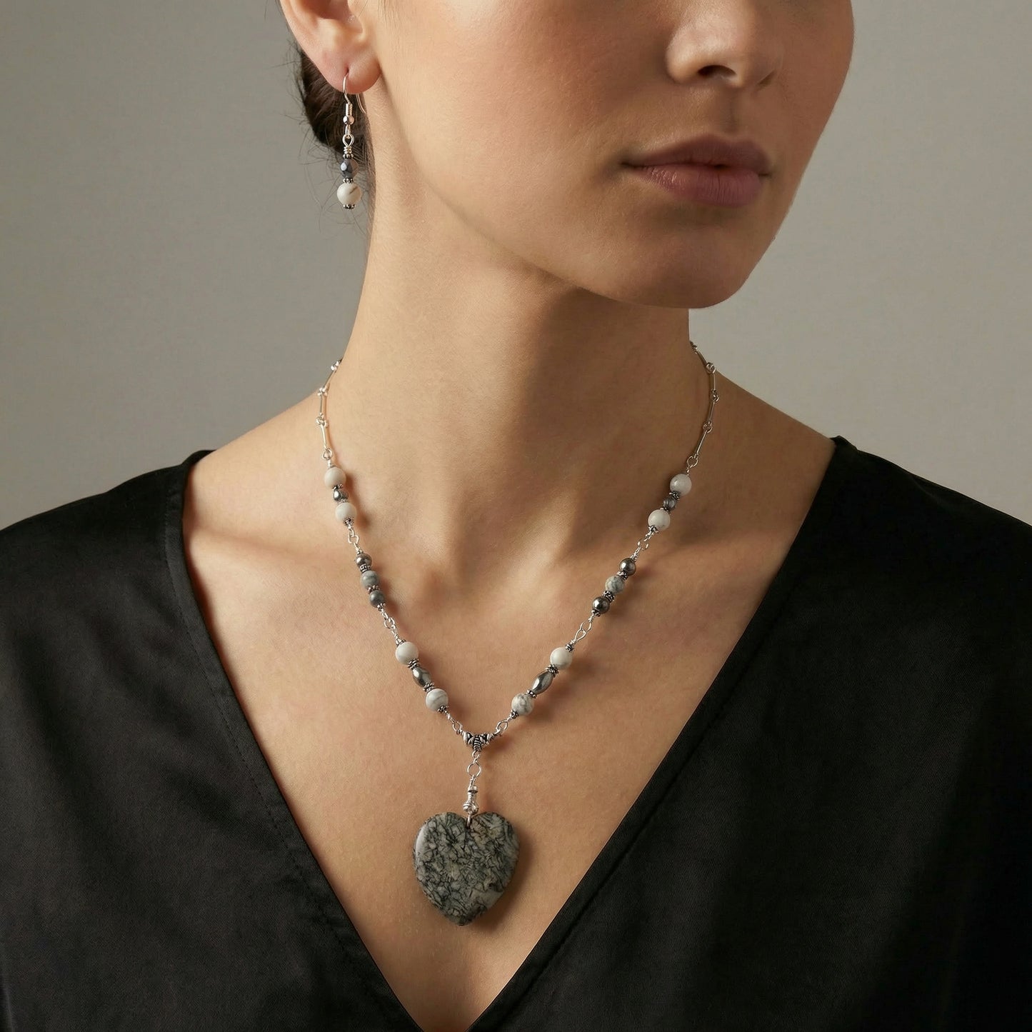 Woman wearing a necklace with a heart-shaped pendant against a neutral background