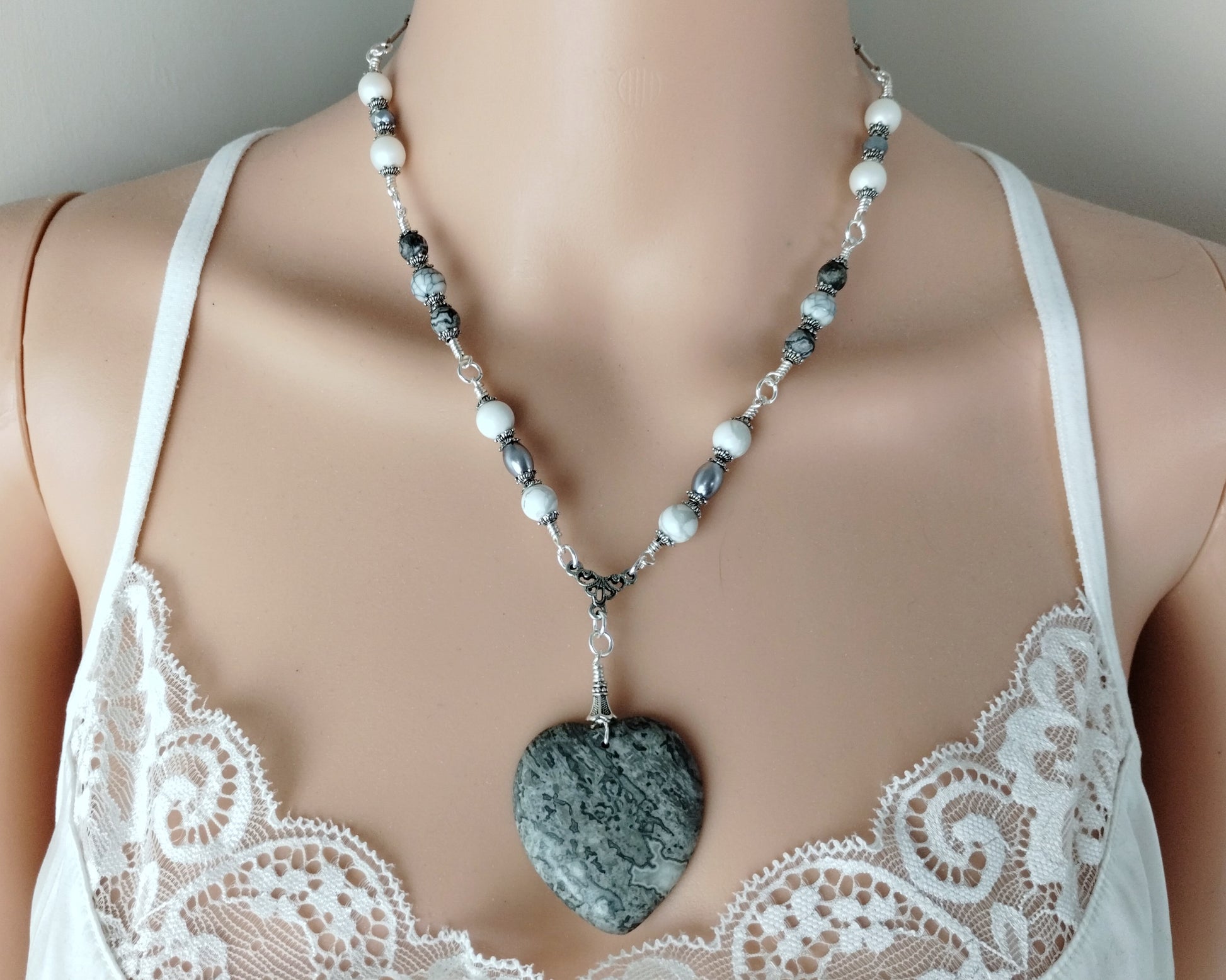 Necklace with a heart-shaped pendant on a mannequin wearing a white lace top.