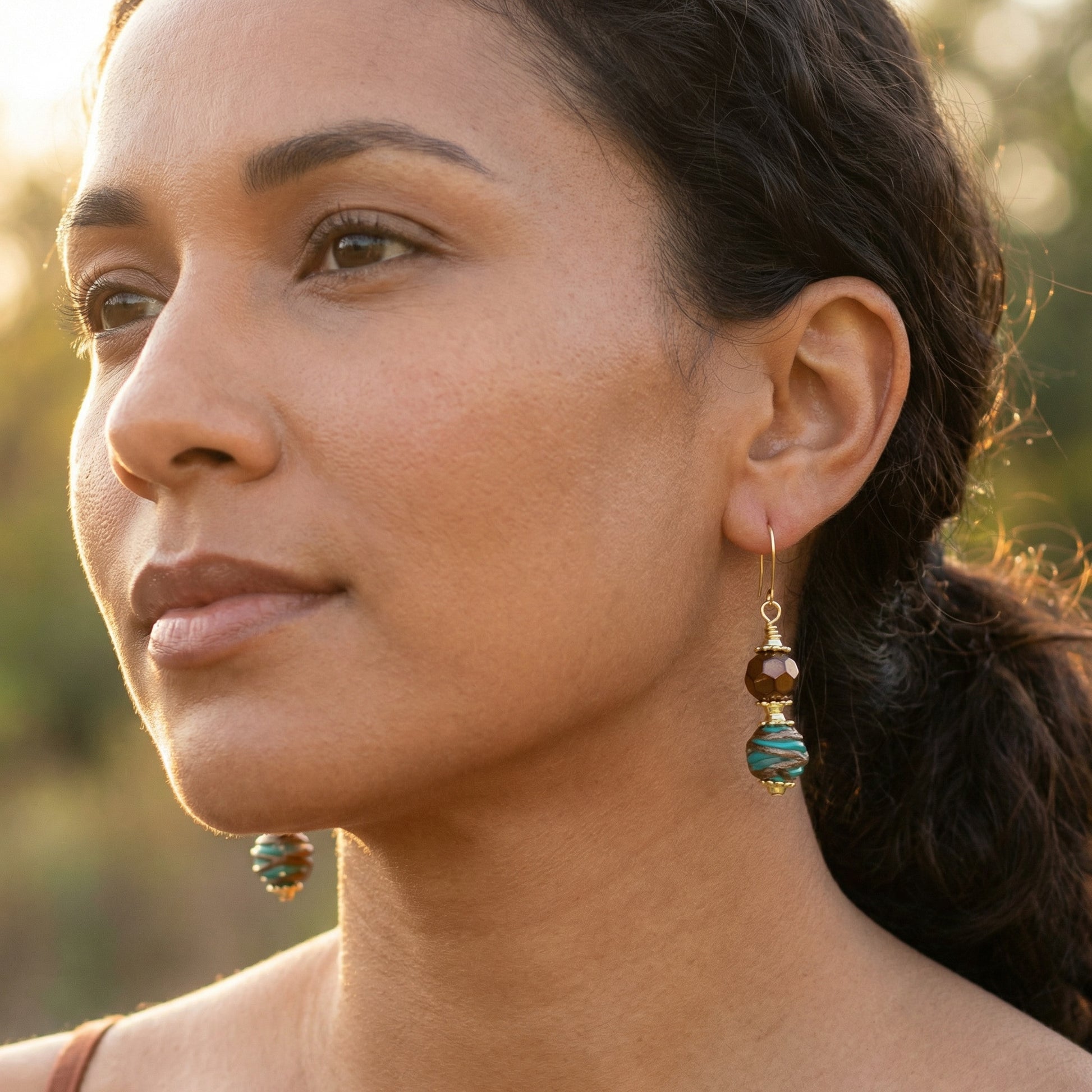 Close-up of a woman wearing gold and turquoise earrings with a blurred natural background