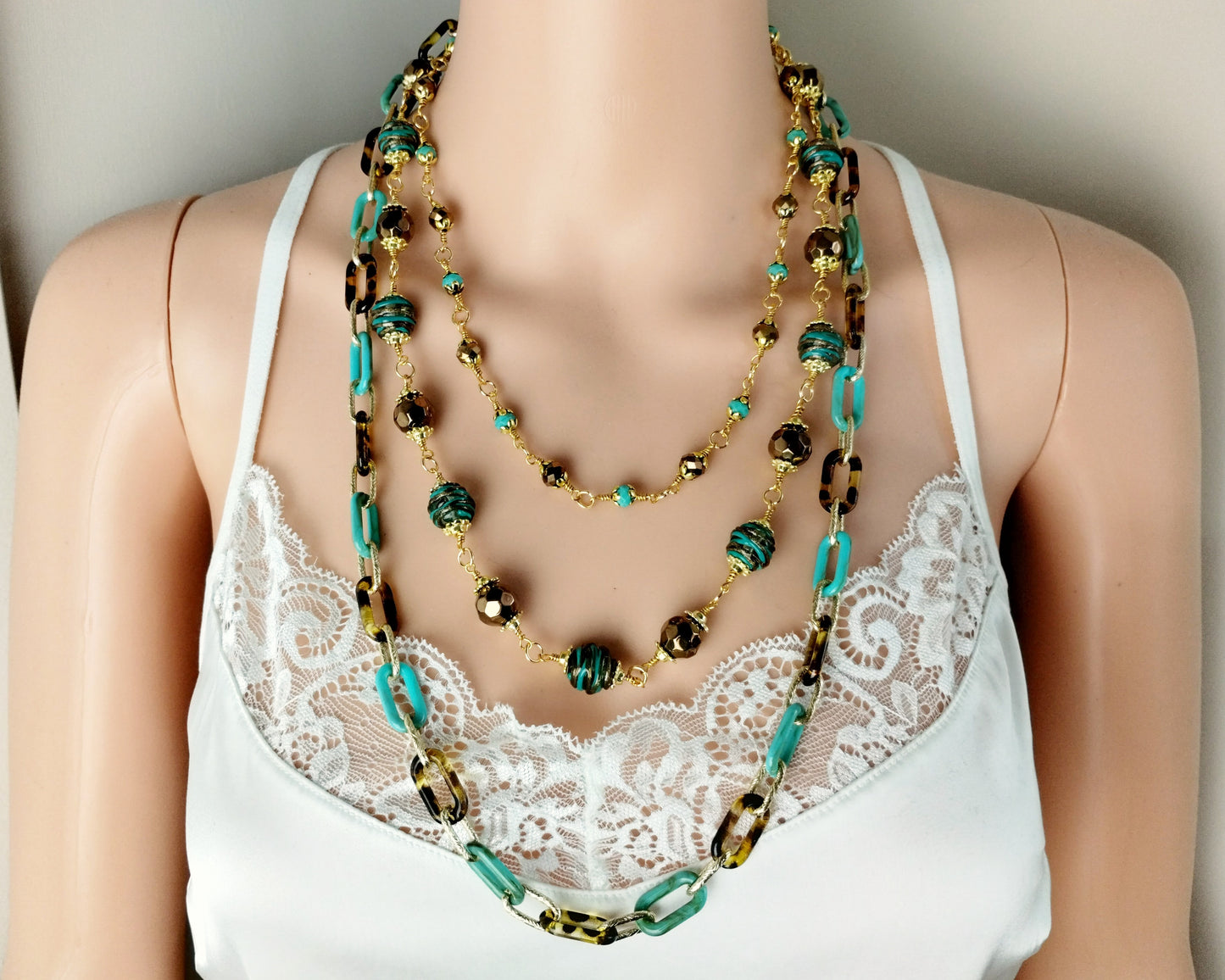 Necklace with green and gold beads on a mannequin wearing a white lace top.