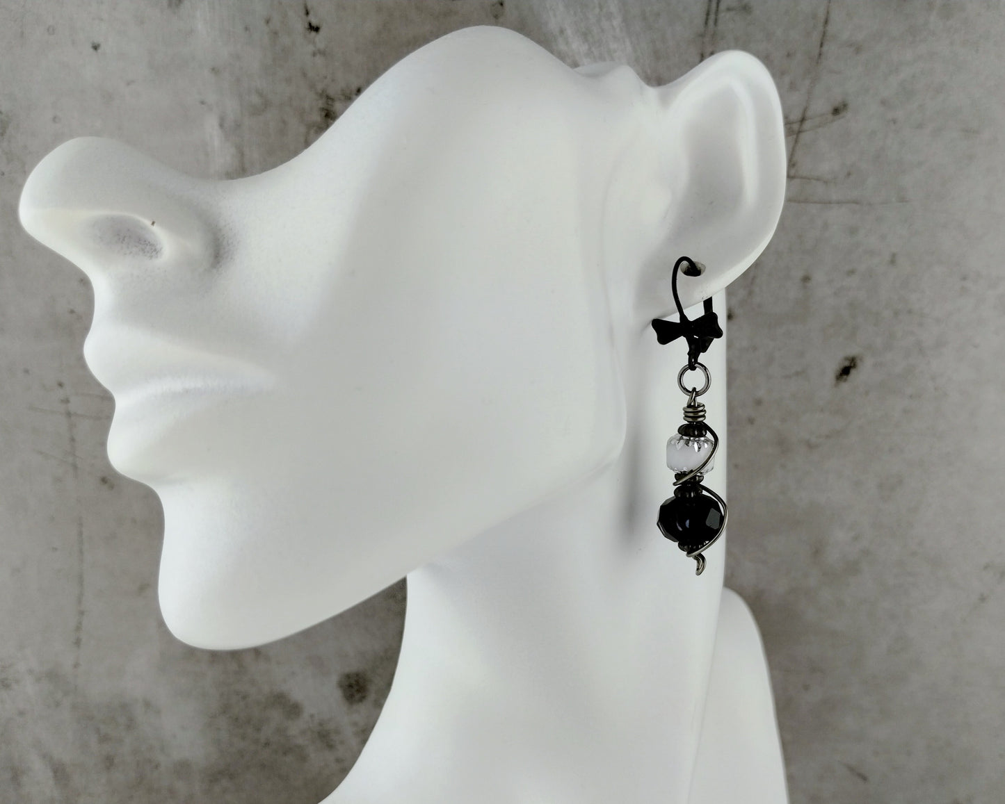 Bow tie lever back black and white earrings on a bust.