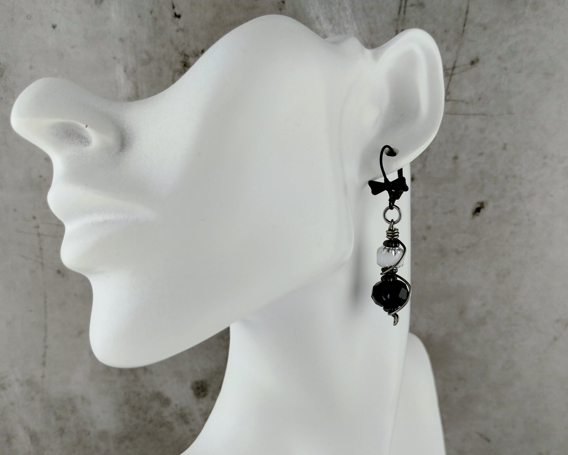 Bow tie lever back black and white earrings on a bust.