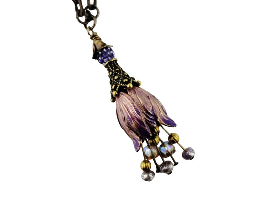 A vintage-style floral tassel pendant necklace featuring purple and lavender enamel petals, antique bronze metalwork, and dangling iridescent beads on a white background.